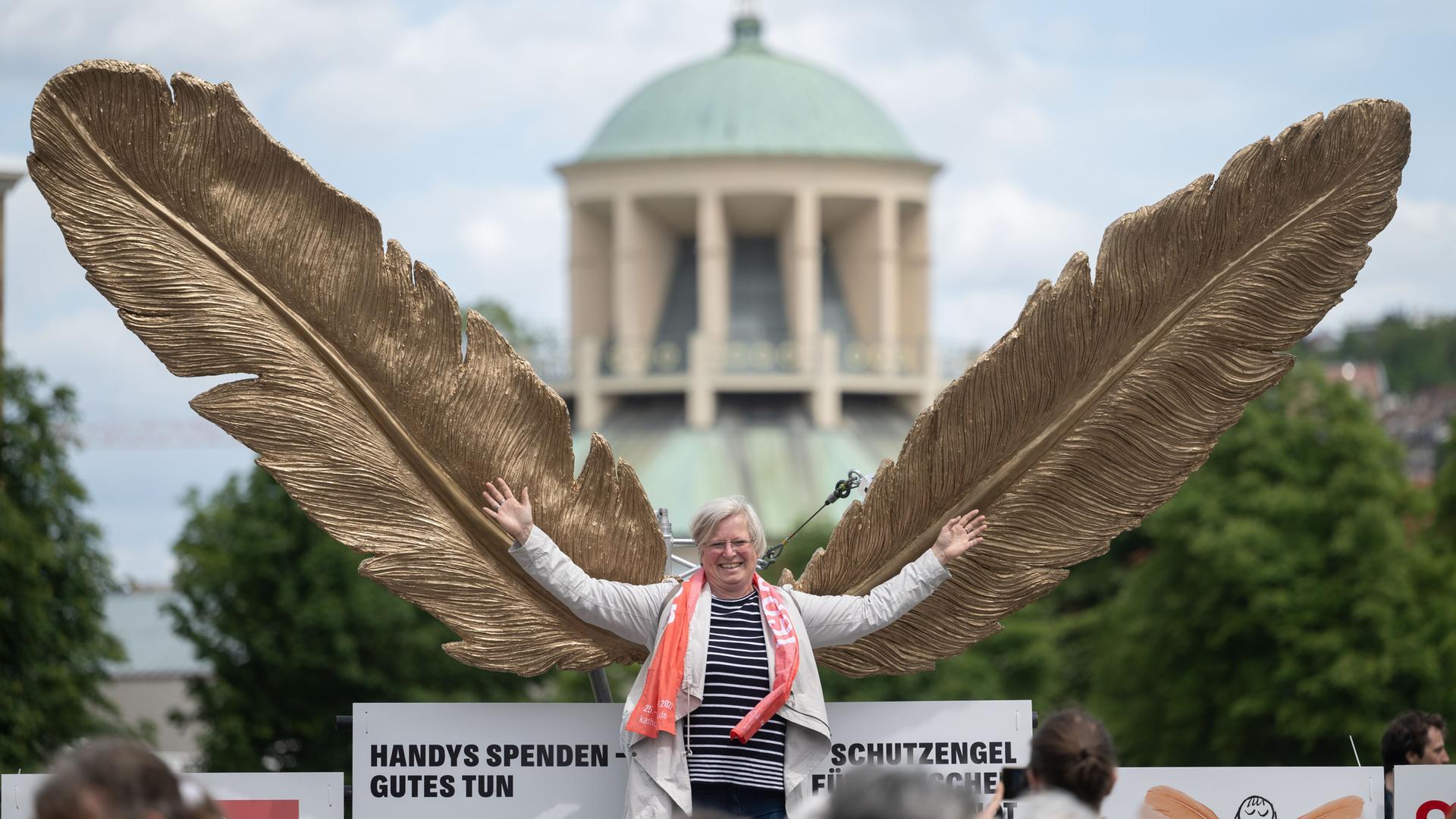 Eine mittelalte Frau schwingt lachend riesige goldene Flügel und stellt sich damit als einen "Schutzengel" dar. Eine mittelalte Frau schwingt lachend riesige goldene Flügel und stellt sich damit als einen "Schutzengel" dar.