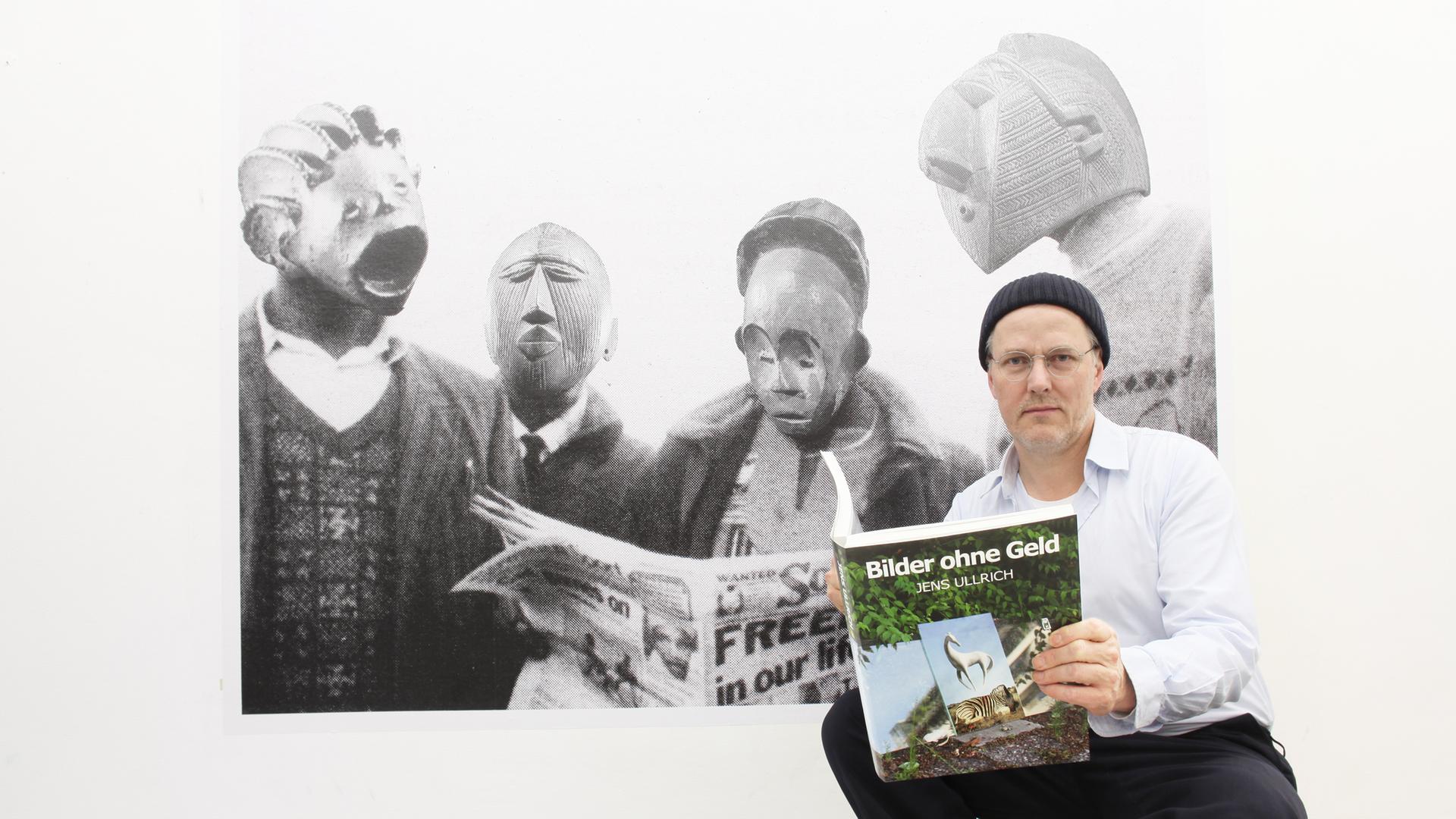 Der Künstler Jens Ullrich steht vor einem großformatigen Foto, das Menschen mit Masken zeigt Der Künstler Jens Ullrich steht vor einem großformatigen Foto, das Menschen mit Masken zeigt