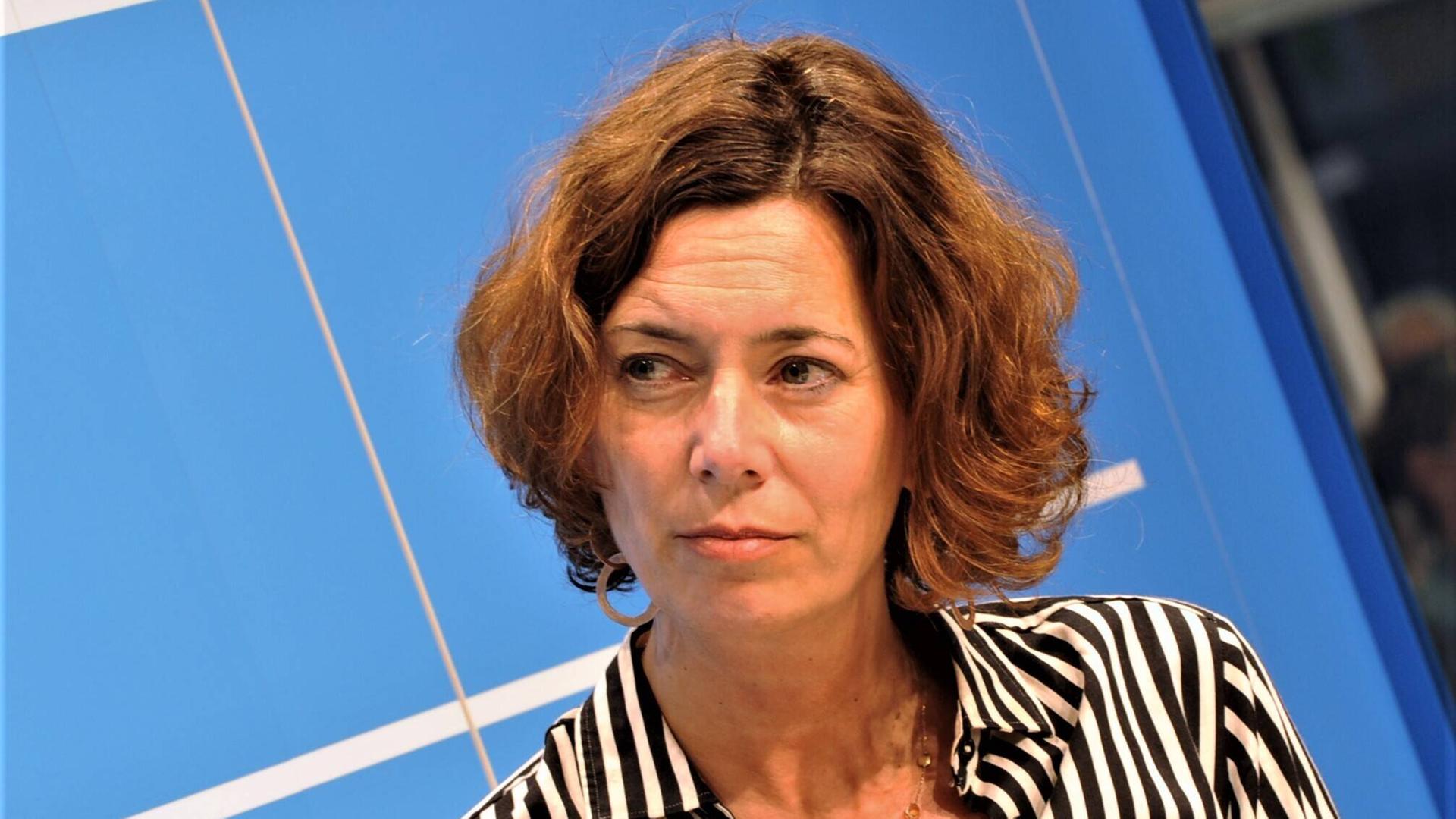 Journalistin und Autorin Eva Menasse. Eine Frau mit halblangen braunen Haaren sitzt auf einem Podium. 