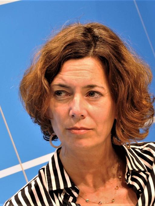 Journalistin und Autorin Eva Menasse. Eine Frau mit halblangen braunen Haaren sitzt auf einem Podium. 