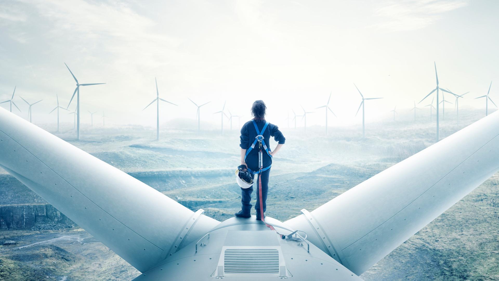 Eine Frau im Blaumann steht auf der Turbine eines Windrades und schaut aufs aufgewühlte Meer. Eine Frau im Blaumann steht auf der Turbine eines Windrades und schaut aufs aufgewühlte Meer.