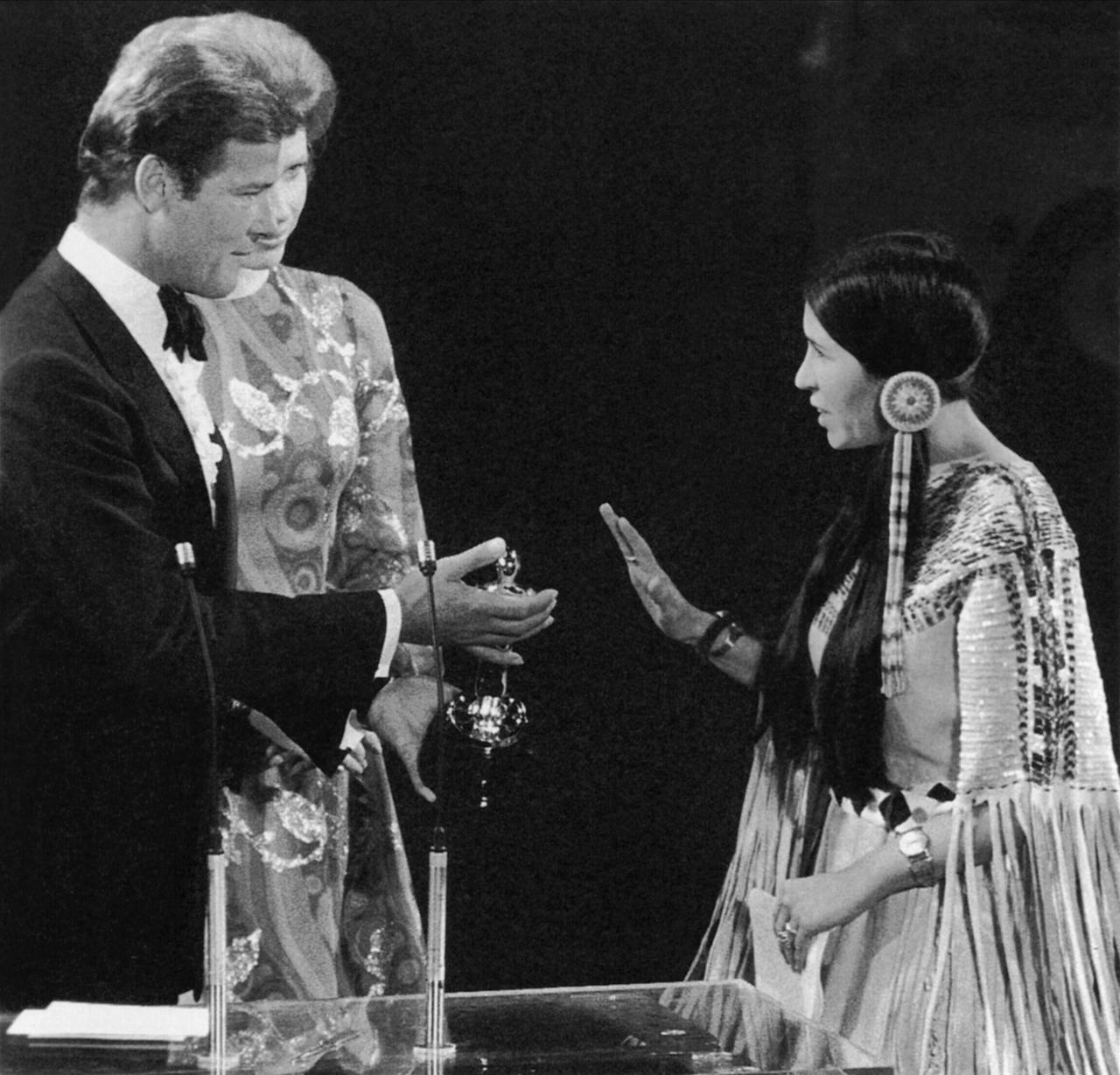 45. Academy Awards: Am 27.03.1973 lehnt Sacheen Littlefeather stellvertretend für Marlon Brando den Oscar ab. Daneben stehen Roger Moore und Liv Ullmann.