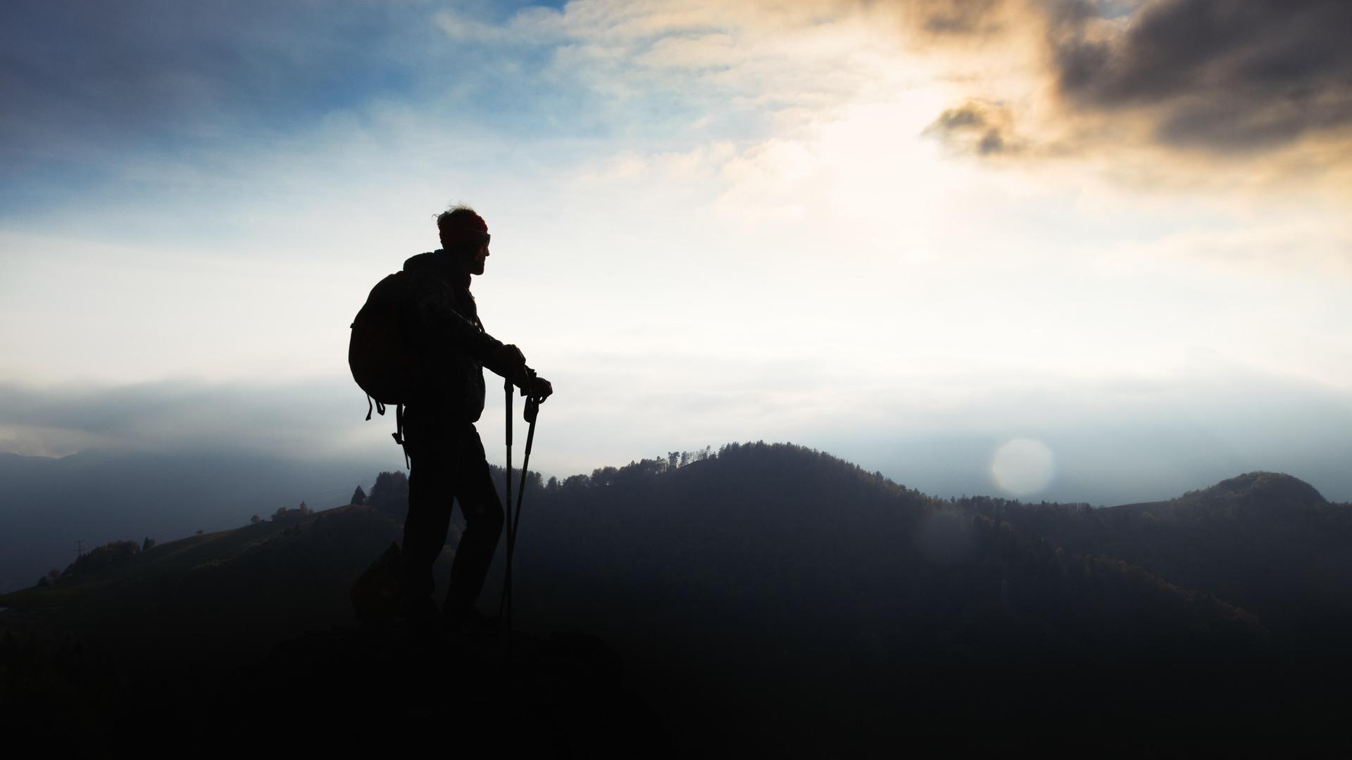 Ein Mann mit Walking-Stöcken steht auf einem Berg bei Sonnenuntergang Ein Mann mit Walking-Stöcken steht auf einem Berg bei Sonnenuntergang
