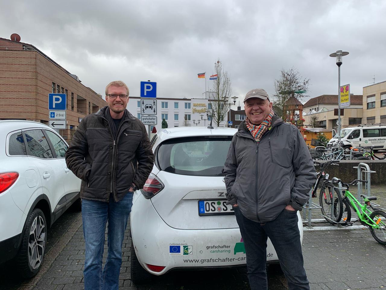 Zwei Männer stehen vor einem kleinen Elektro-PKW, der die Aufschrift "Grafschafter Carsharing" trägt. Zwei Männer stehen vor einem kleinen Elektro-PKW, der die Aufschrift "Grafschafter Carsharing" trägt.