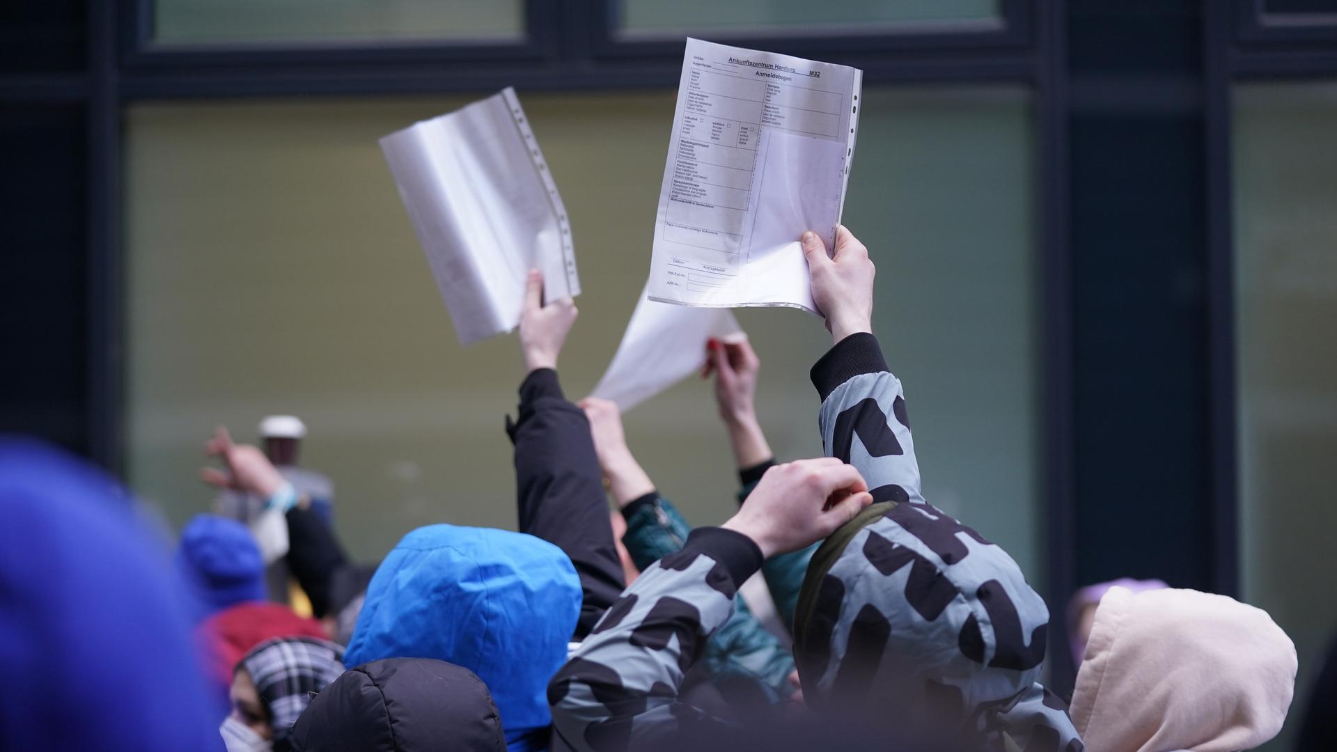 Flüchtlinge halten Formulare in einer Warteschlange vor einer Ausländerbehörde hoch. Flüchtlinge halten Formulare in einer Warteschlange vor einer Ausländerbehörde hoch.