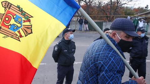 Ein älterer Mann mit der Flagge Moldaus, im Hintergrund steht ein Polizist.