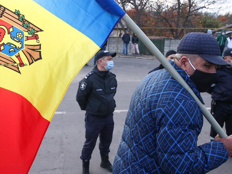 Ein älterer Mann mit der Flagge Moldaus, im Hintergrund steht ein Polizist.