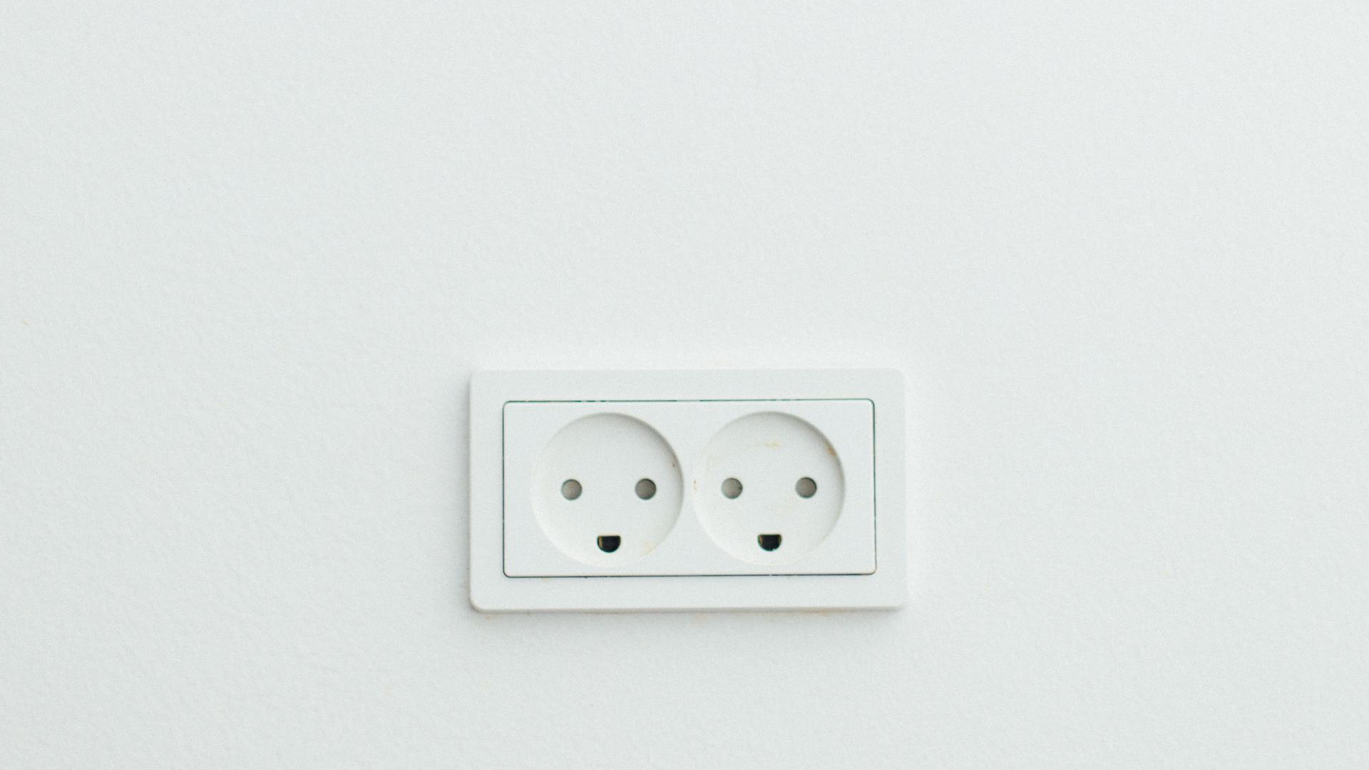 Eine Doppelsteckdose auf weißer Wand. Sie erinnert an Smileys. Eine Doppelsteckdose auf weißer Wand. Sie erinnert an Smileys.