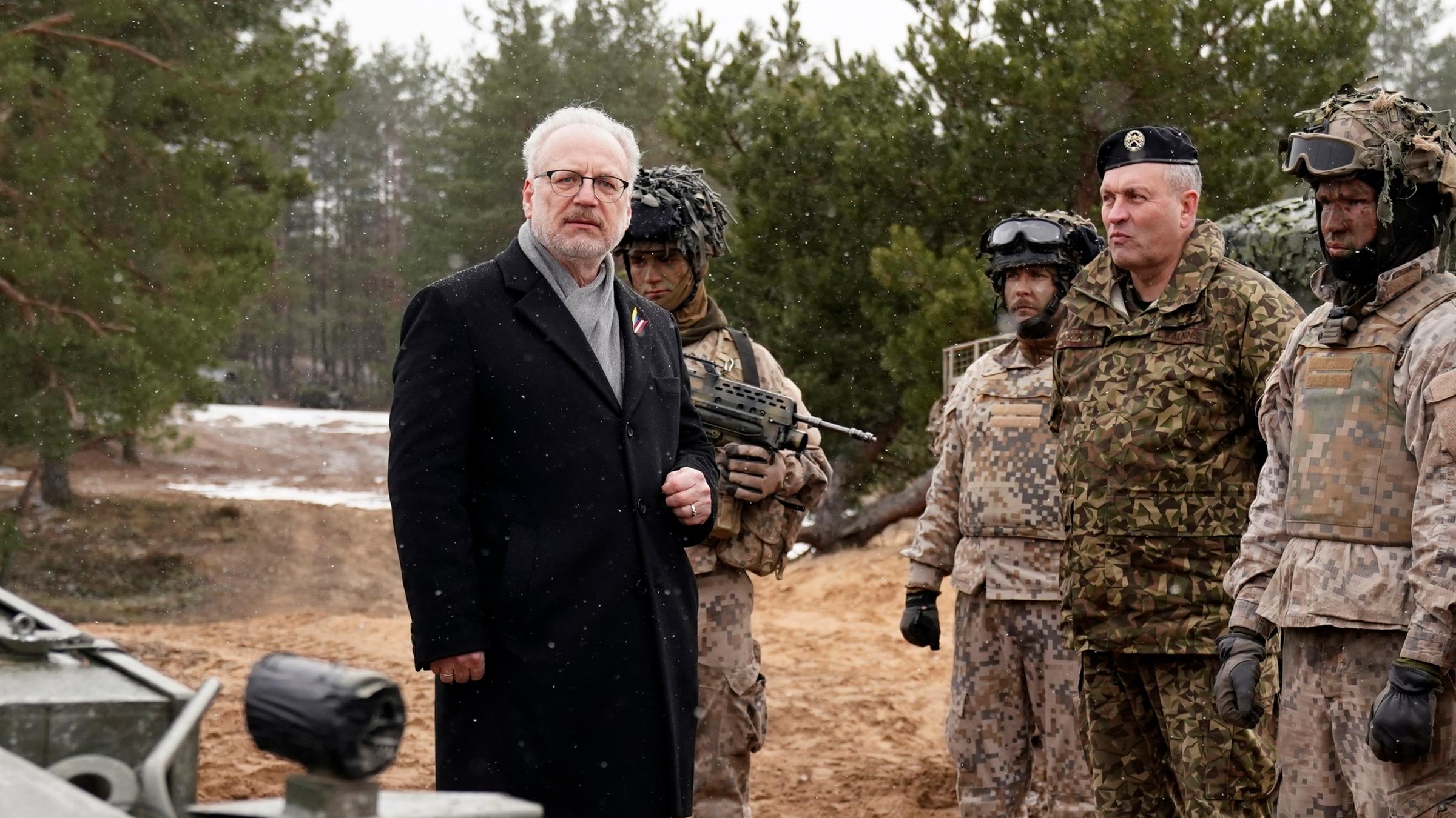Der lettische Staatspräsident Egils Levits steht neben Soldaten auf einem Übungsfeld