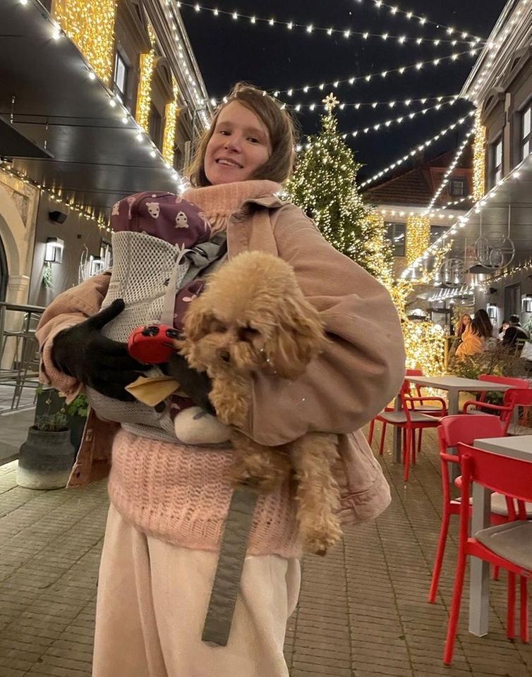Eine junge Frau steht mit Hund und Gepäch im Arm in einer abendlich beleuchteten Straße. Eine junge Frau steht mit Hund und Gepäch im Arm in einer abendlich beleuchteten Straße.