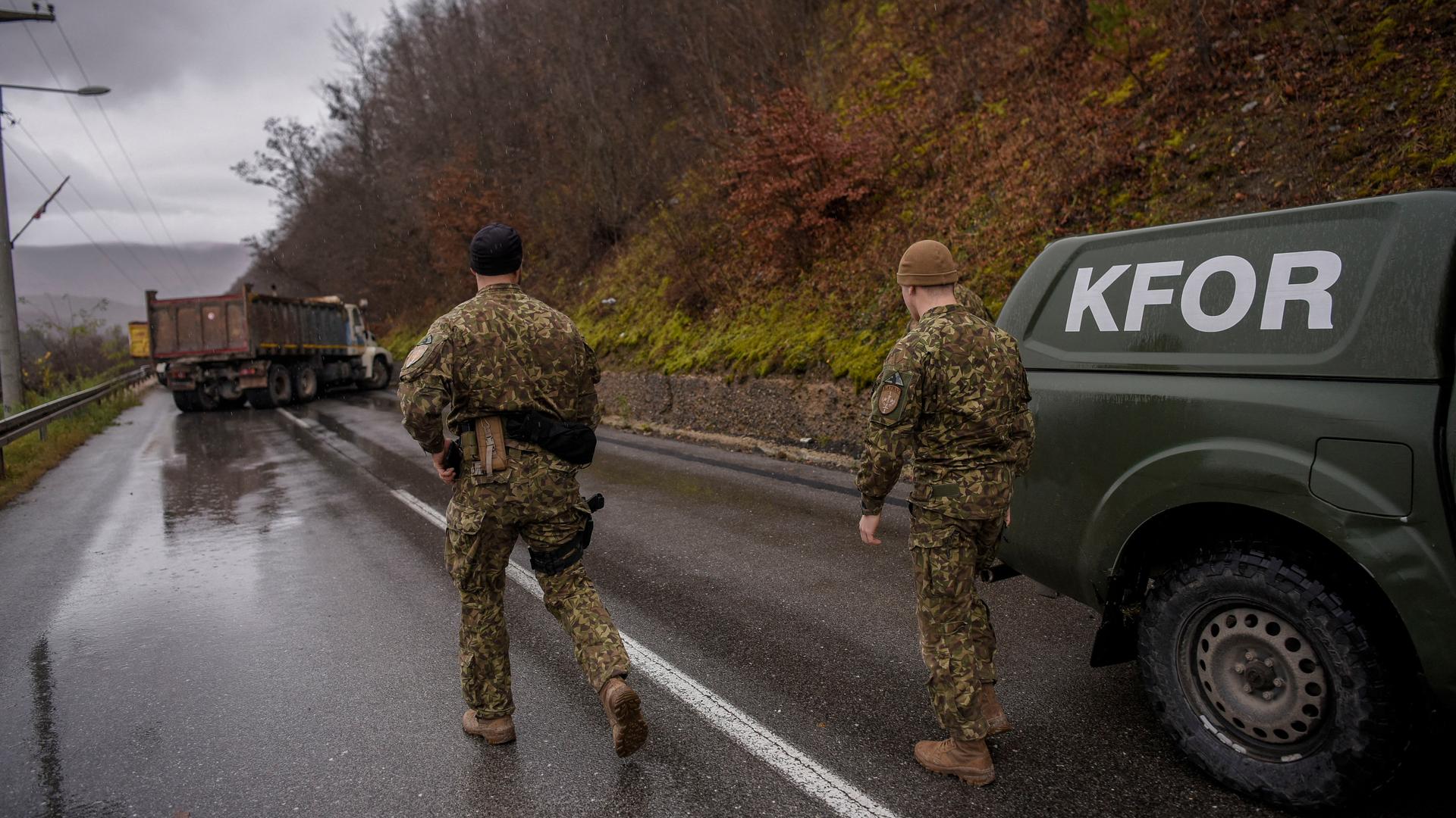 Soldaten der NATO-geführten KFOR-Truppe gehen über eine Straße, die von einem Lastwagen blockiert ist. Soldaten der NATO-geführten KFOR-Truppe gehen über eine Straße, die von einem Lastwagen blockiert ist.