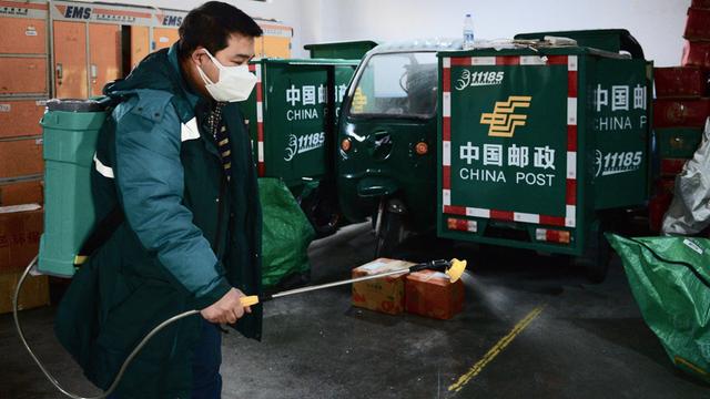 Xi'an, Chian: Ein Post-Mitarbeiter versprüht Desinfektionsmittel in einem Warenhaus. Im Hintergrund stehen Postfahrzeuge.