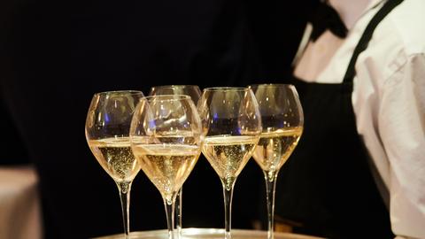 Tablett mit gefüllten Champagnergläsern wird gehalten von einer Servicekraft mit weißem Hemd und schwarzer Fliege