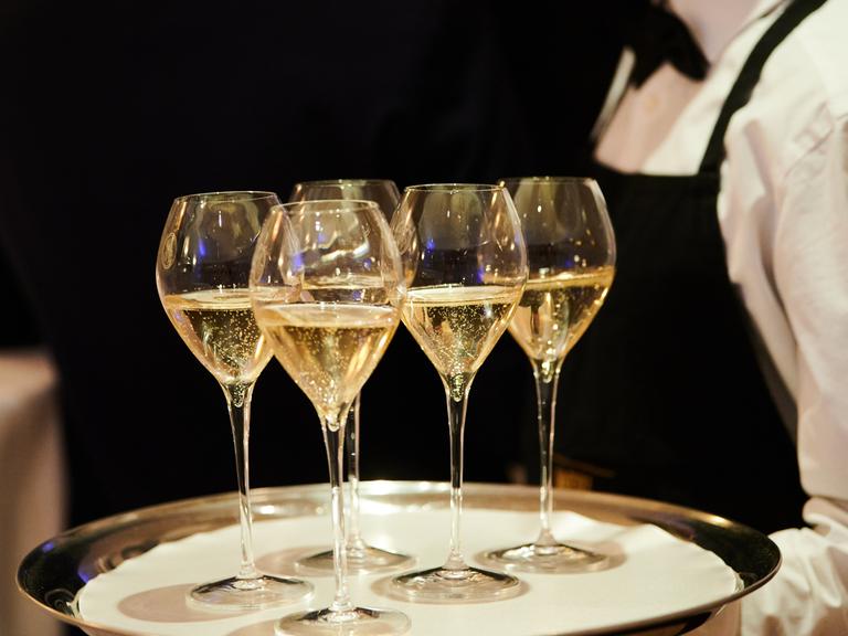 Tablett mit gefüllten Champagnergläsern wird gehalten von einer Servicekraft mit weißem Hemd und schwarzer Fliege