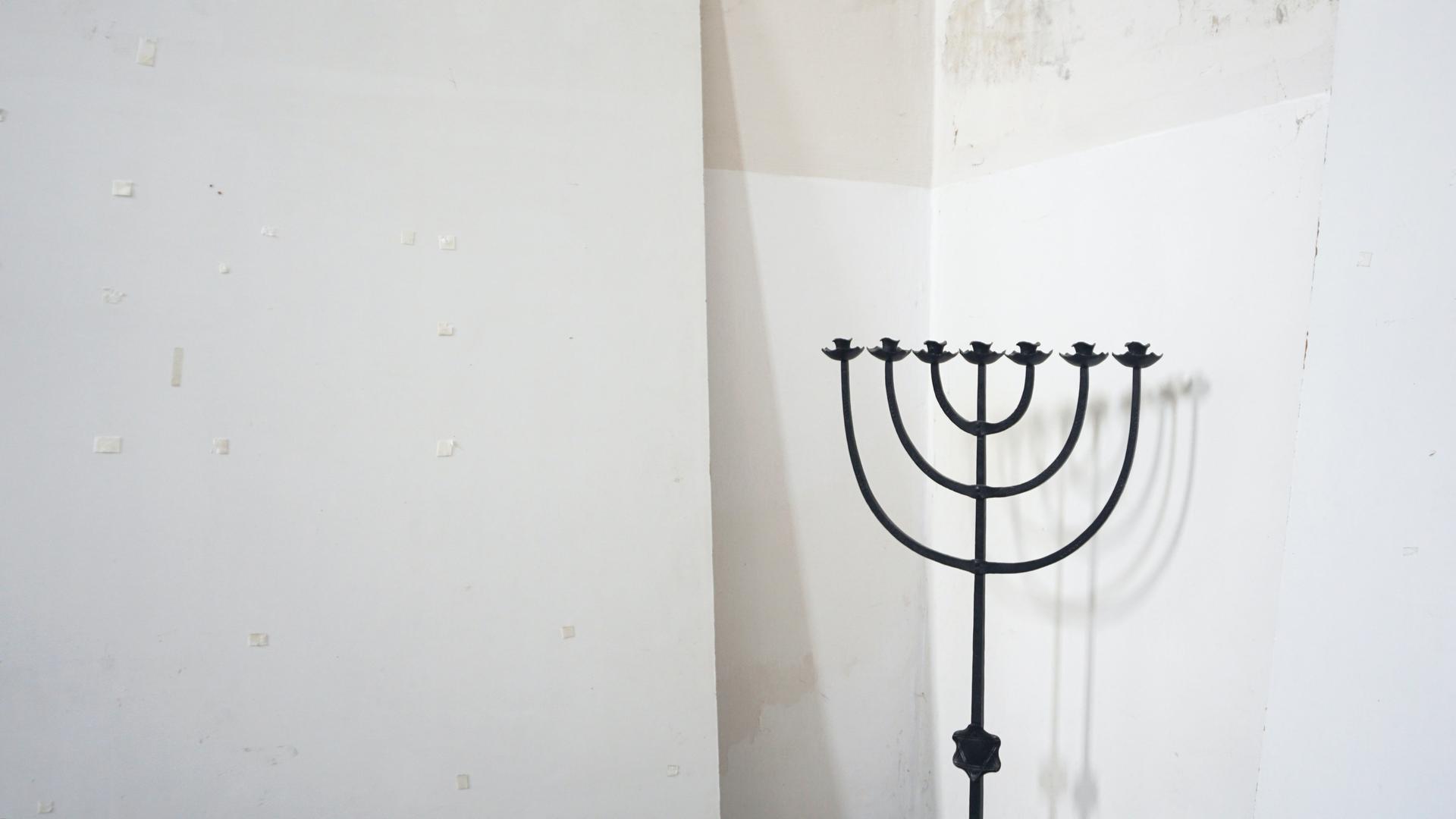 Eine siebenarmige schwarze Menorah steht vor einer weißen Wand. Eine siebenarmige schwarze Menorah steht vor einer weißen Wand.