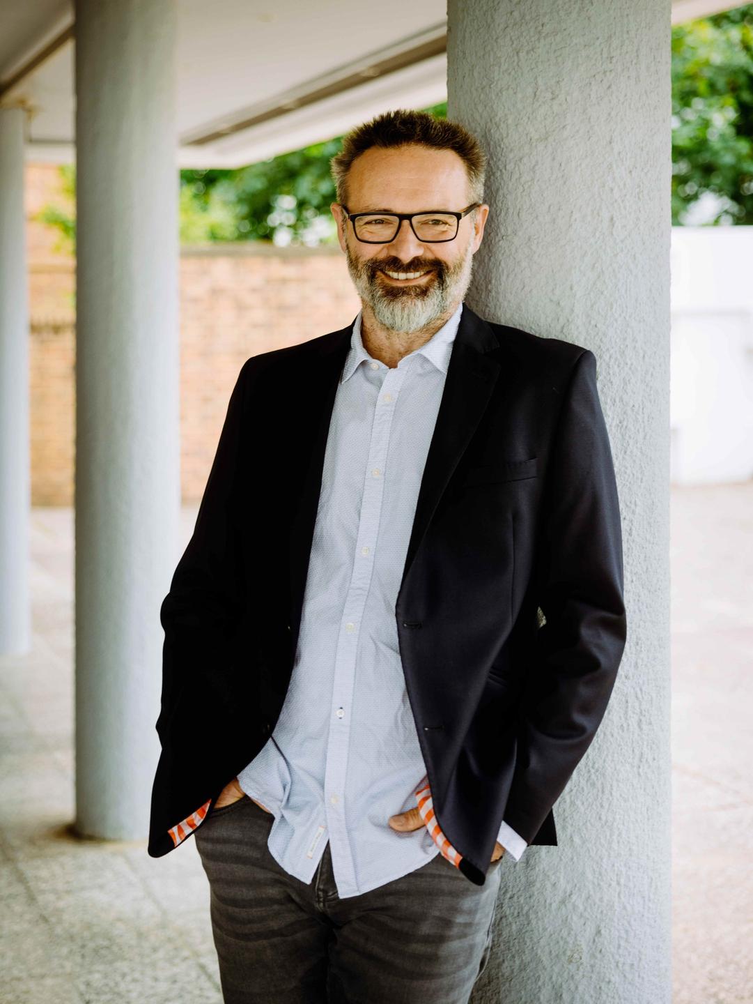 Der Intendant des Volkstheaters Rostock, Ralph Reichel, lehnt an einer Säule und lächelt entspannt in die Kamera. Der Intendant des Volkstheaters Rostock, Ralph Reichel, lehnt an einer Säule und lächelt entspannt in die Kamera.
