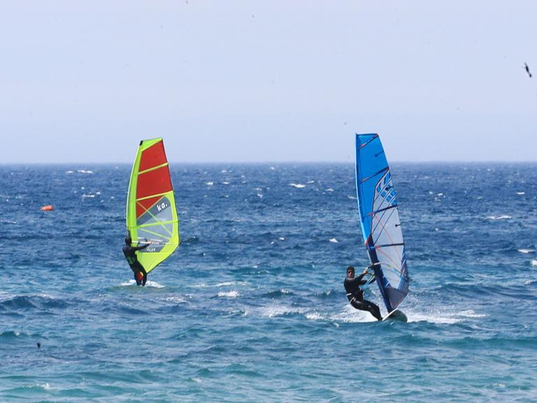 Zwei Windsurfer stehen auf ihrem Board und surfen auf dem Meer.