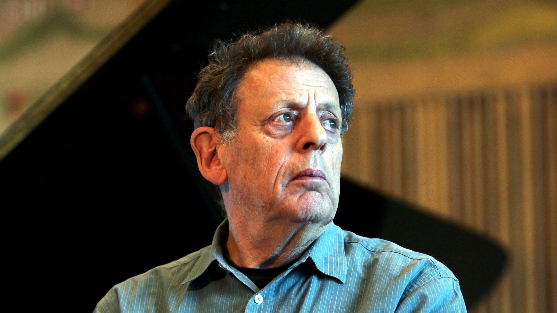 Philip Glass sitzt vor einem aufgeklappten Flügel und schaut nach rechts an der Kamera vorbei. Philip Glass sitzt vor einem aufgeklappten Flügel und schaut nach rechts an der Kamera vorbei.
