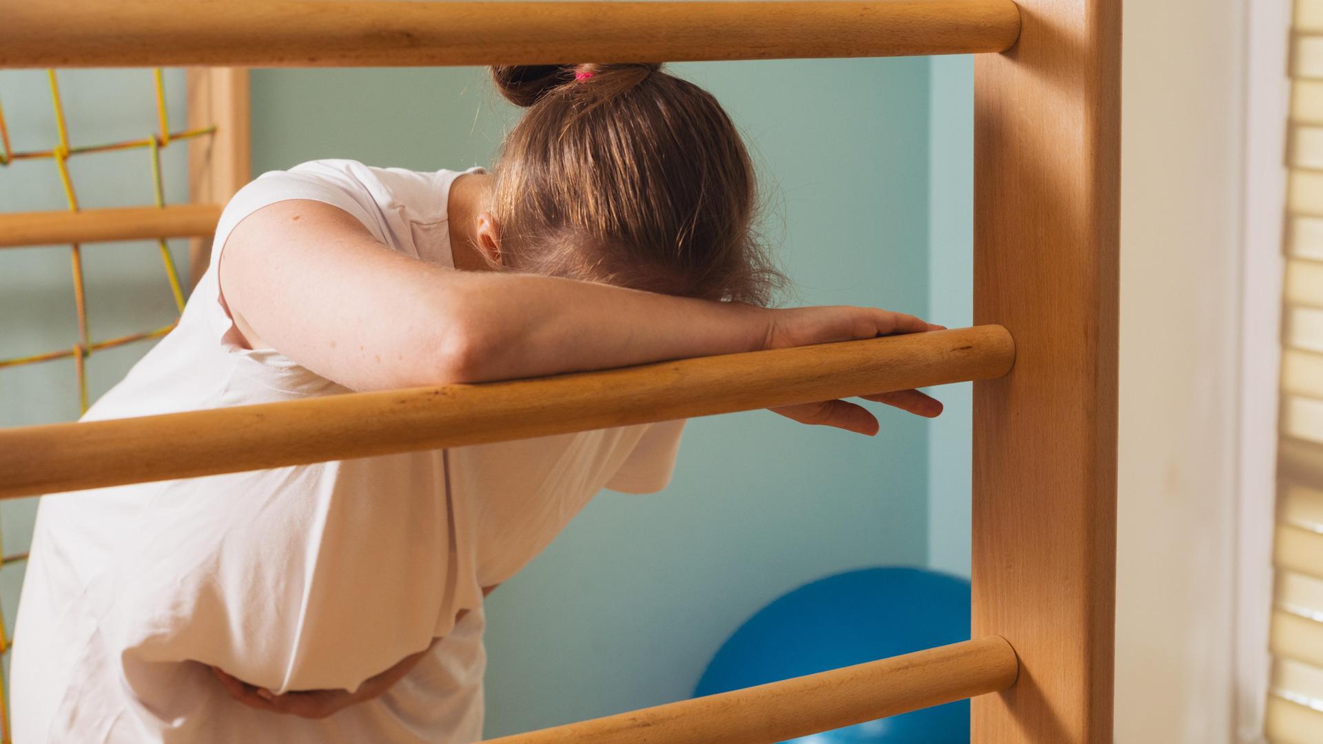 Eine schwangere Frau lehnt in einem Kreißsaal an einer Sprossenwand und stützt den Kopf vor Schmerzen auf den Arm. (Symbolbild) Eine schwangere Frau lehnt in einem Kreißsaal an einer Sprossenwand und stützt den Kopf vor Schmerzen auf den Arm. (Symbolbild)