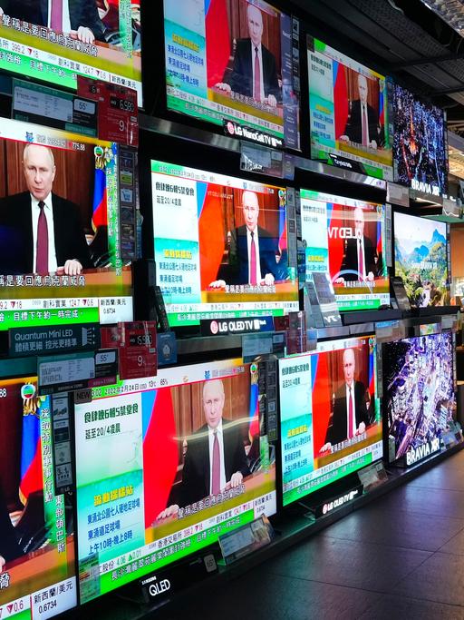 Menschen in Hongkong schauen auf mehrere Fernsehbildschirme, auf denen Putin zu sehen ist.