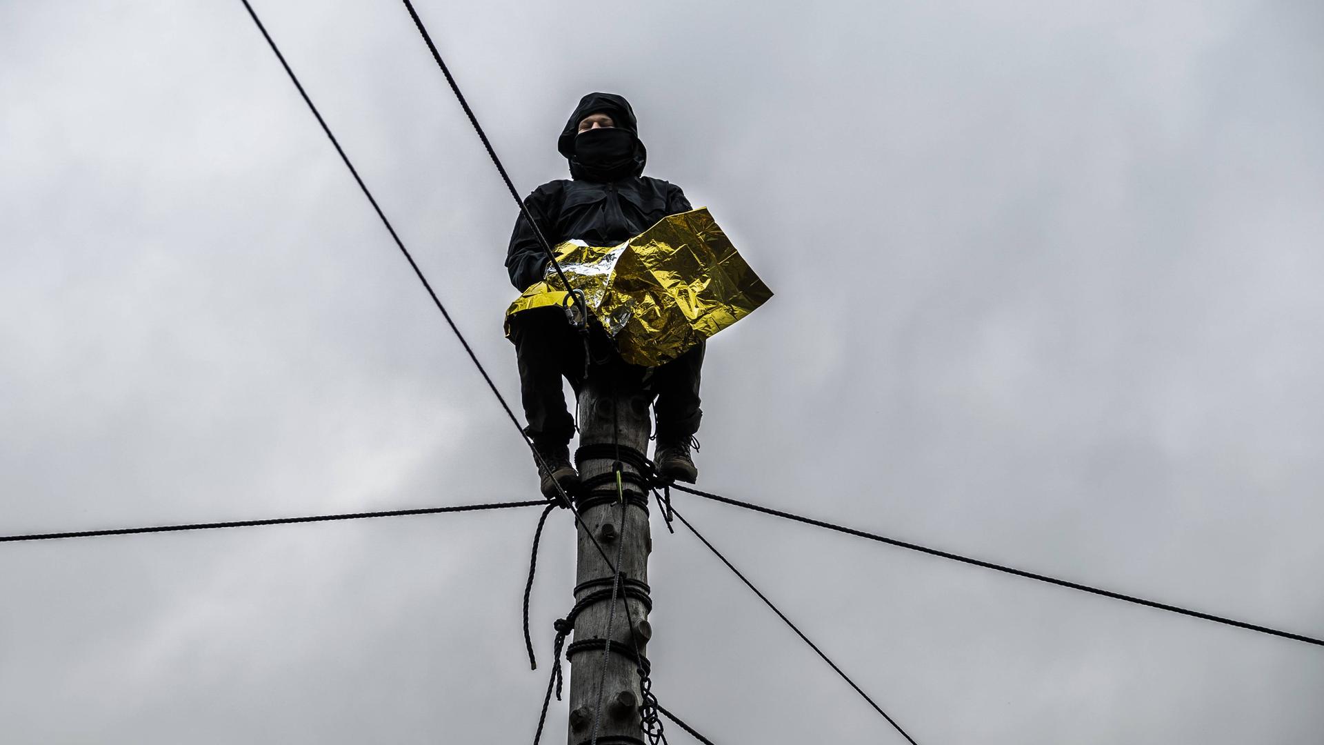 Ein Klimakativist sitzt in Lützerath auf einem Pfahl, gesichert mit Seilen Ein Klimakativist sitzt in Lützerath auf einem Pfahl, gesichert mit Seilen