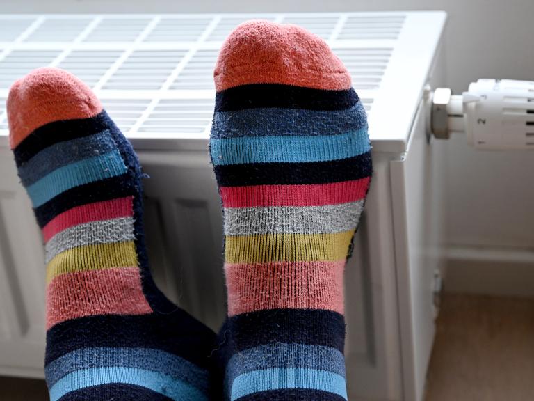 Füße in geringelten Socken liegen zum Wärmen auf einem Heizkörper in einer Wohnung.