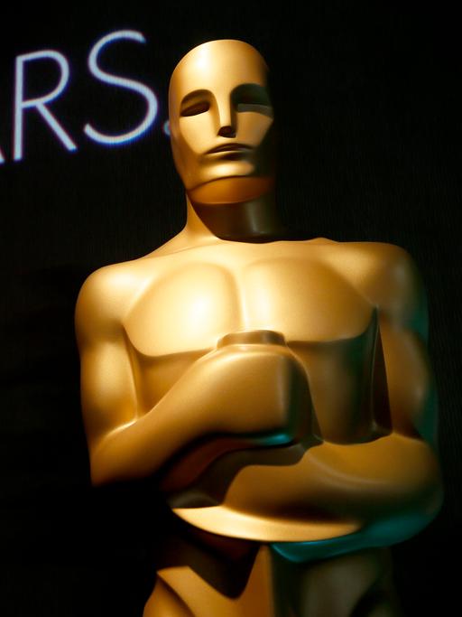 Eine große Oscar-Figur im Hintergrund steht auf einer schwarzen Wand "Oscars"