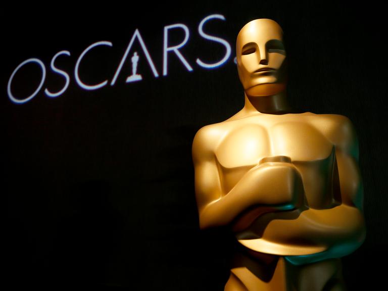 Eine große Oscar-Figur im Hintergrund steht auf einer schwarzen Wand "Oscars"