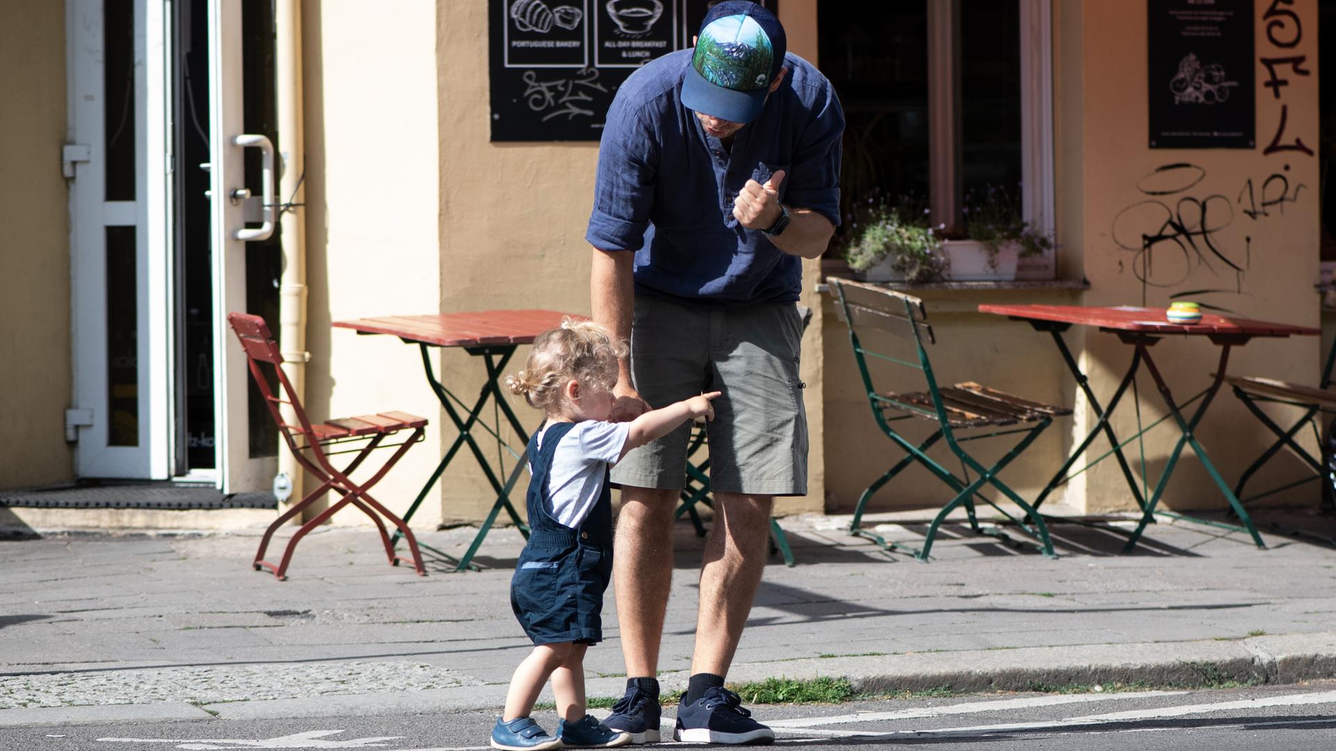 Ein Vater übt mit seinem Kind, wie man sicher die Straße überqueren kann. 