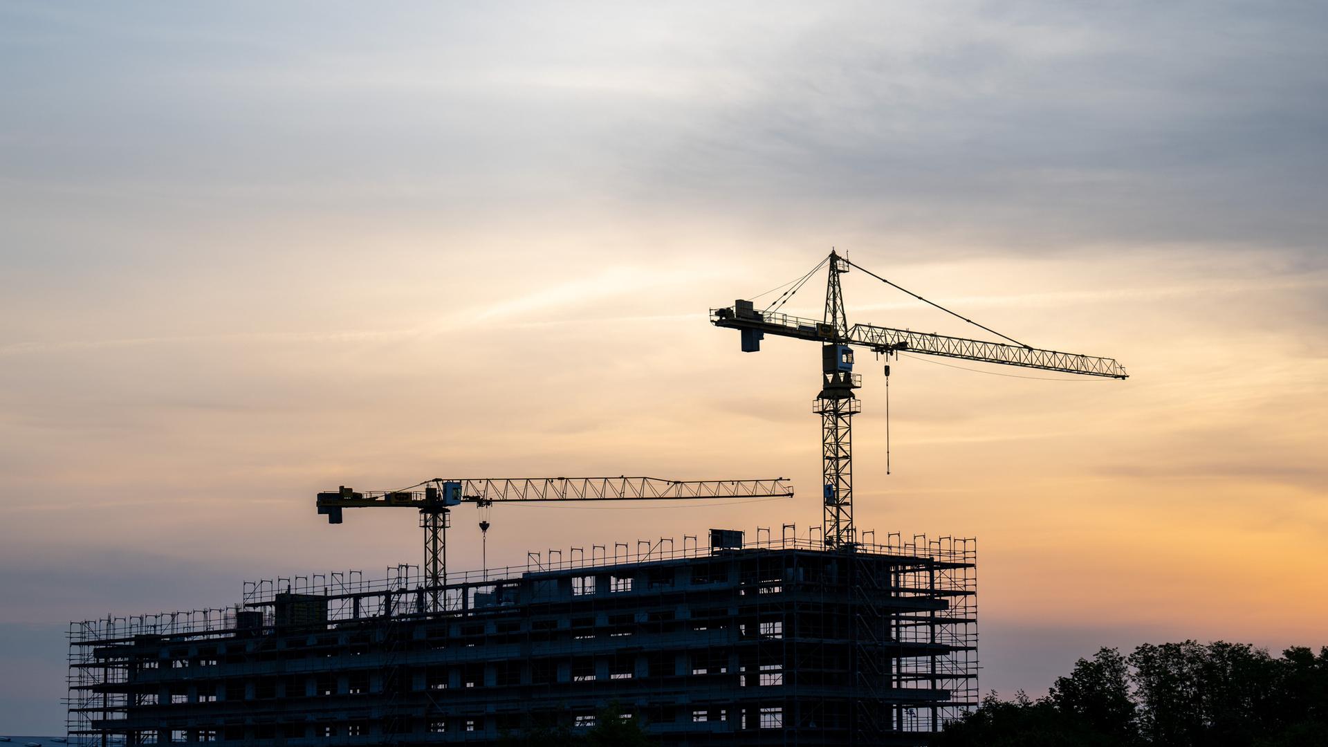 Baustelle bei Sonnenaufgang mit zwei Kränen.