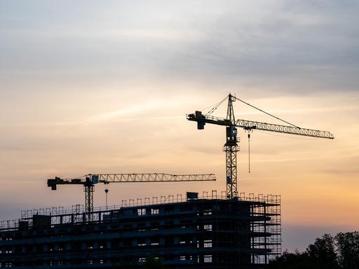 Baustelle bei Sonnenaufgang mit zwei Kränen.