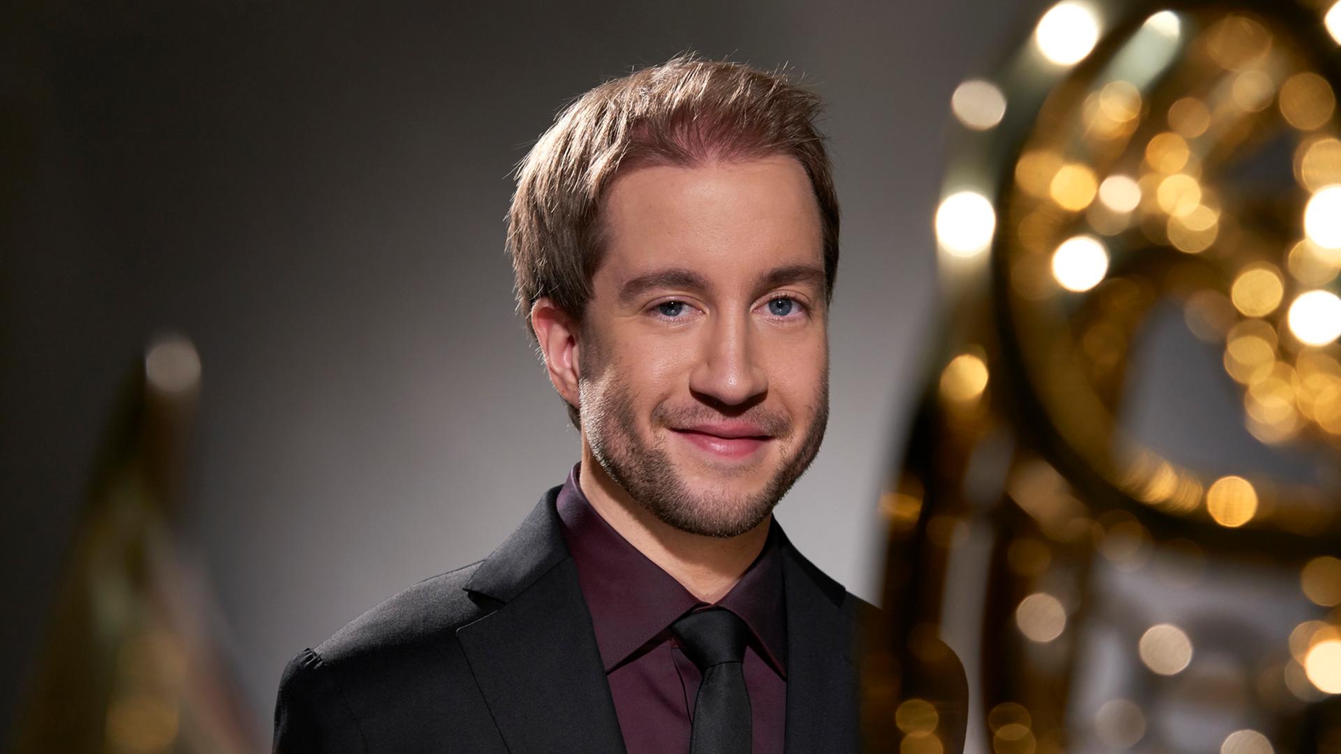 Ein junger Mann, Felix Klieser, schaut in die Kamera, vor der ein großes Horn liegt und deshalb unscharf glitzert. Ein junger Mann, Felix Klieser, schaut in die Kamera, vor der ein großes Horn liegt und deshalb unscharf glitzert.