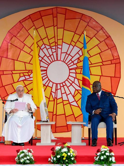 Papst Franziskus sitzt neben dem Präsidenten der Demokratischen Republik Kongo, Felix Tshiseke vor einem bunten Sonnenbild. 