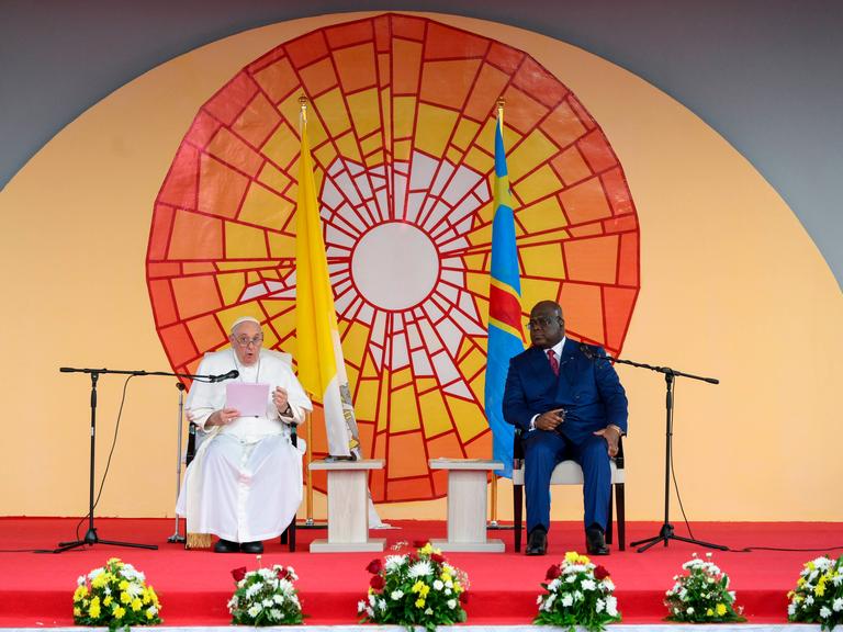 Papst Franziskus sitzt neben dem Präsidenten der Demokratischen Republik Kongo, Felix Tshiseke vor einem bunten Sonnenbild. 