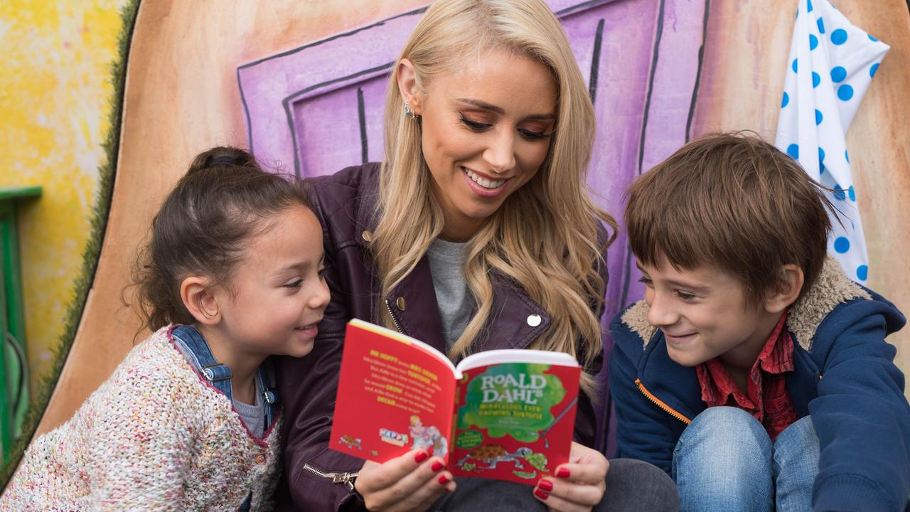 Eine blonde Frau liest zwei Kindern aus einem Buch von Roald Dahl vor.