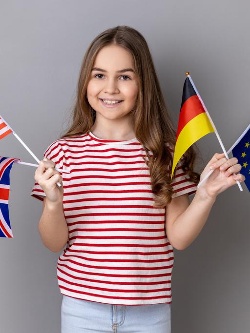 Ein lächelndes Mädchen hält die Fahnen Deutschlands, Großbritanniens, der USA und der Europäischen Union.