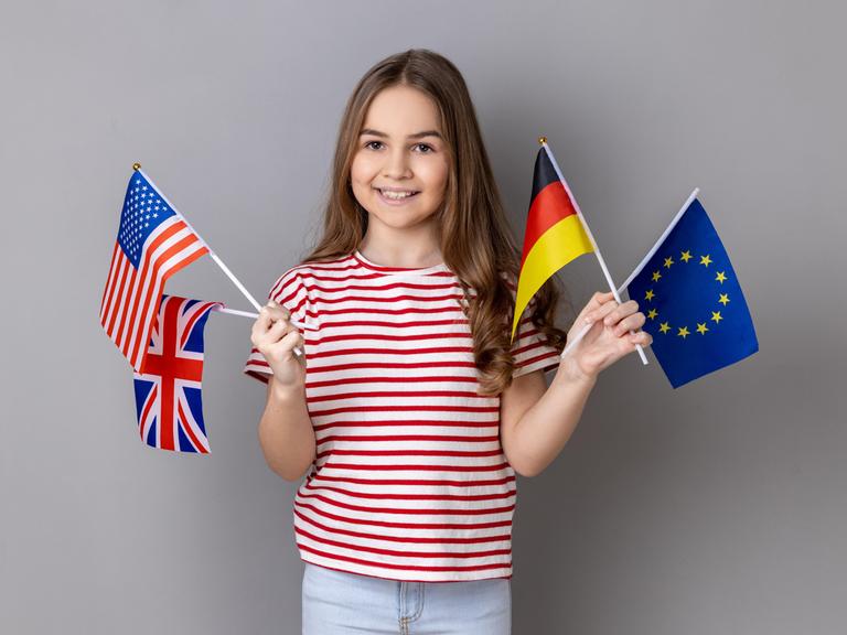 Ein lächelndes Mädchen hält die Fahnen Deutschlands, Großbritanniens, der USA und der Europäischen Union.