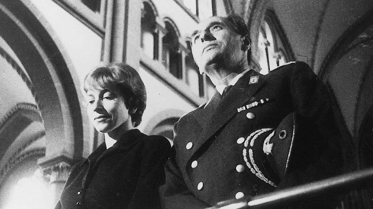 Filmszene aus "Machorka-Muff", hier mit Renate Lang und Erich Kuby. Beide stehen andächtig in einer Kirche und sind von unten zu sehen. Filmszene aus "Machorka-Muff", hier mit Renate Lang und Erich Kuby. Beide stehen andächtig in einer Kirche und sind von unten zu sehen.
