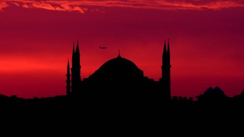 Die Shilouette der Hagia Sophia in Istanbul vor einem blutroten Himmel, an dem ein Flugzeug zu sehen ist.
