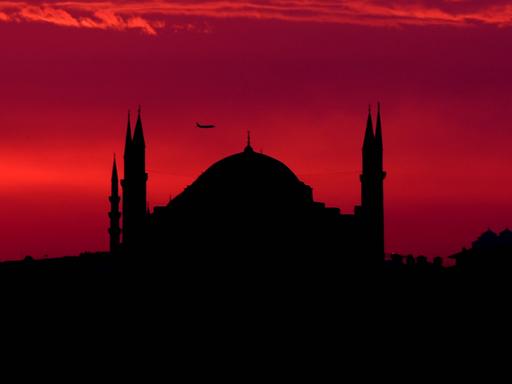 Die Shilouette der Hagia Sophia in Istanbul vor einem blutroten Himmel, an dem ein Flugzeug zu sehen ist.