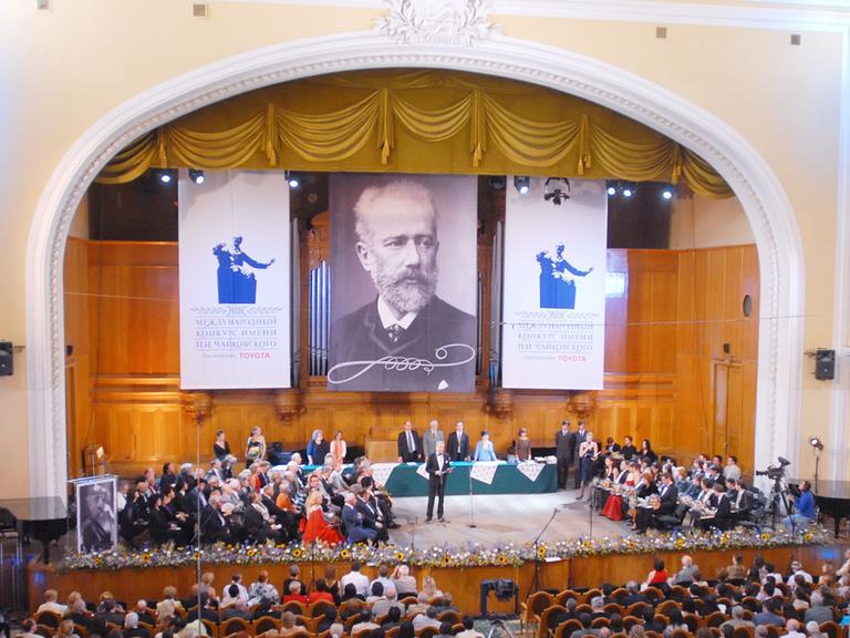 Die Bühne mit Teilnehmern des Internationalen Tschaikowsky-Wettbewerbs in Moskau, darüber ein großen Plakat mit dem Bild von Tschaikowsky 