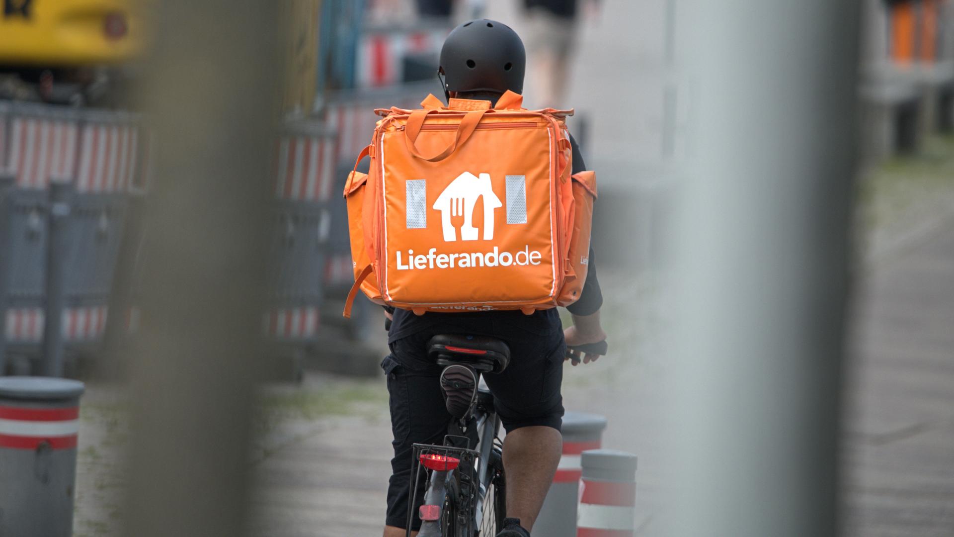 Ein Fahrradkurier des Fastfood-Lieferdienstes Lieferando.de mit Helm im Einsatz. Mit einem großen, orangefarbenen Thermo-Rucksack werden die bestellten Speisen per Fahrrad ausgeliefert.