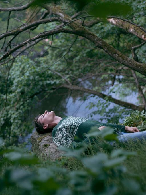 Ein Mann liegt mit geschlossenen Augen im Wald und meditiert.