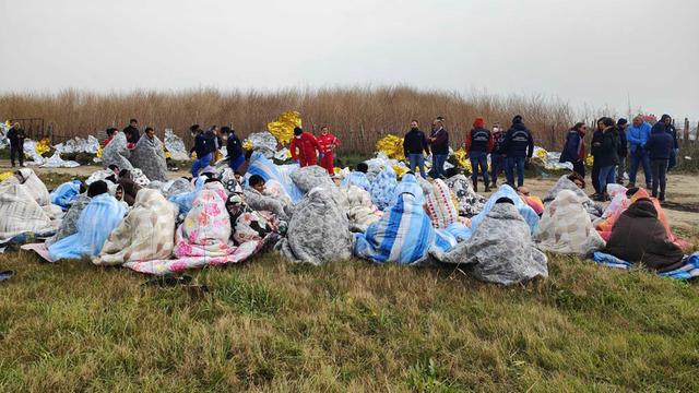 Gerettete Flüchtlinge sitzen in Decken gehüllt an einem Strand.