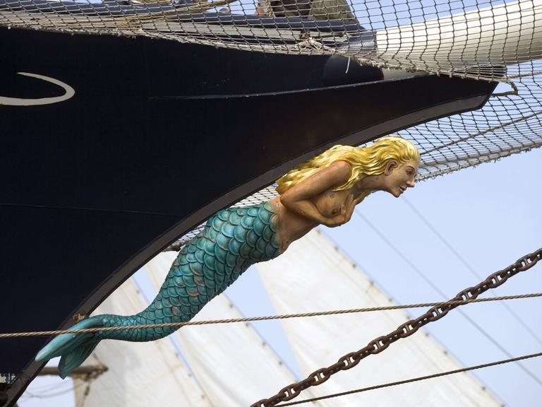Blick auf eine blonde Meerjungfrau aus Holz, die als Galisonsfigur ein Segelschiff ziert.