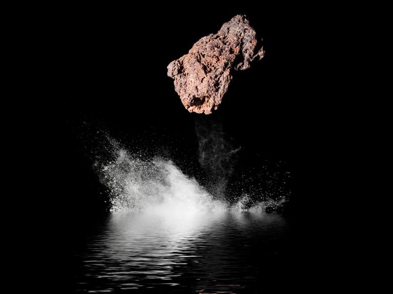 Ein Steinmeteorit aus dem Weltall, er fällt in schwarzes Wasser bei Nacht.