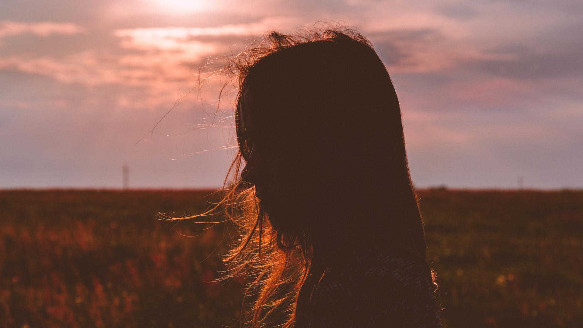 Eine junge Frau im Profil, Wiese und Sonnenuntergang im Hintergrund. Eine junge Frau im Profil, Wiese und Sonnenuntergang im Hintergrund.