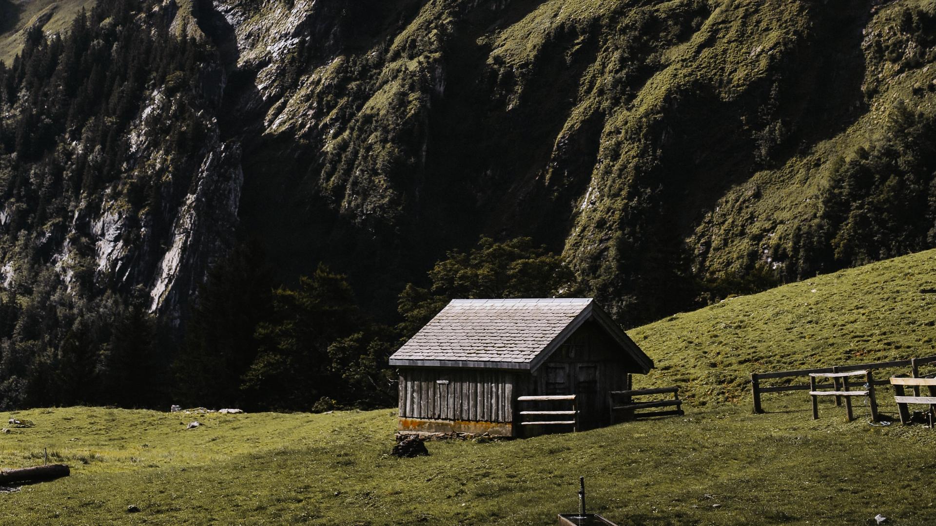 In einer rauen grünen Berglandschaft steht eine vereinzelte Holzhütte. In einer rauen grünen Berglandschaft steht eine vereinzelte Holzhütte.