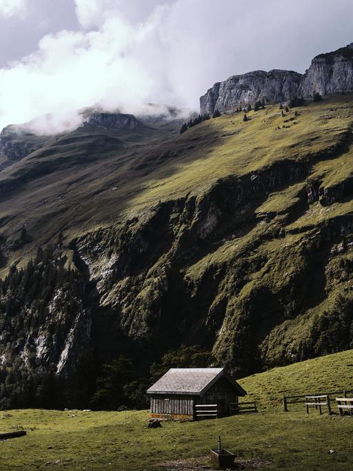 In einer rauen grünen Berglandschaft steht eine vereinzelte Holzhütte.