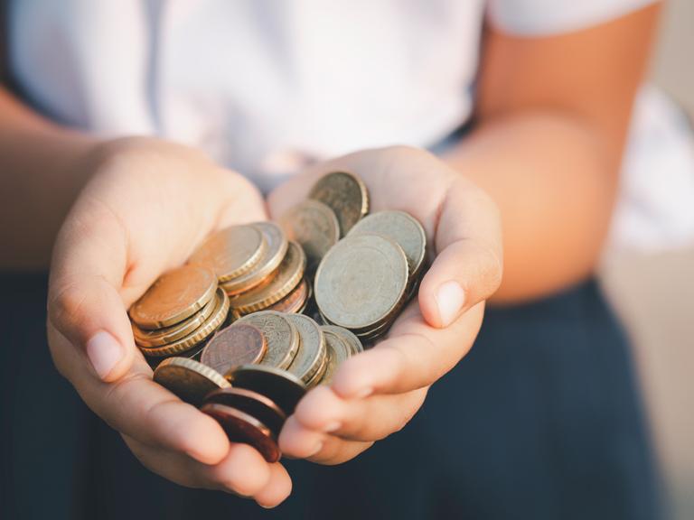 Zu sehen: Eine Frau hält ihre Hände mit Geldmünzen in die Kamera. 